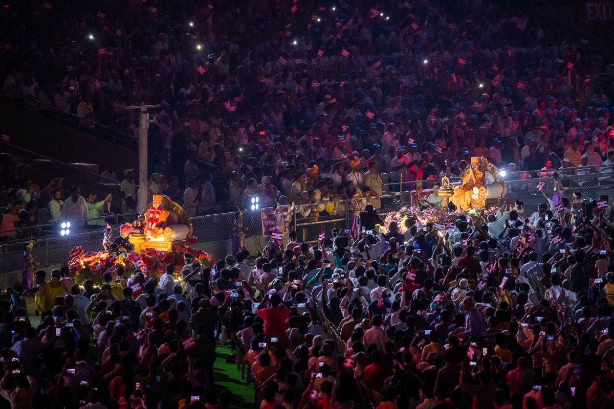 Brahmaswarup Pramukh Swami Maharaj and Pragat Brahmaswarup Mahant Swami Maharaj in a parade on decorated chariots around the perimeter of the stadium