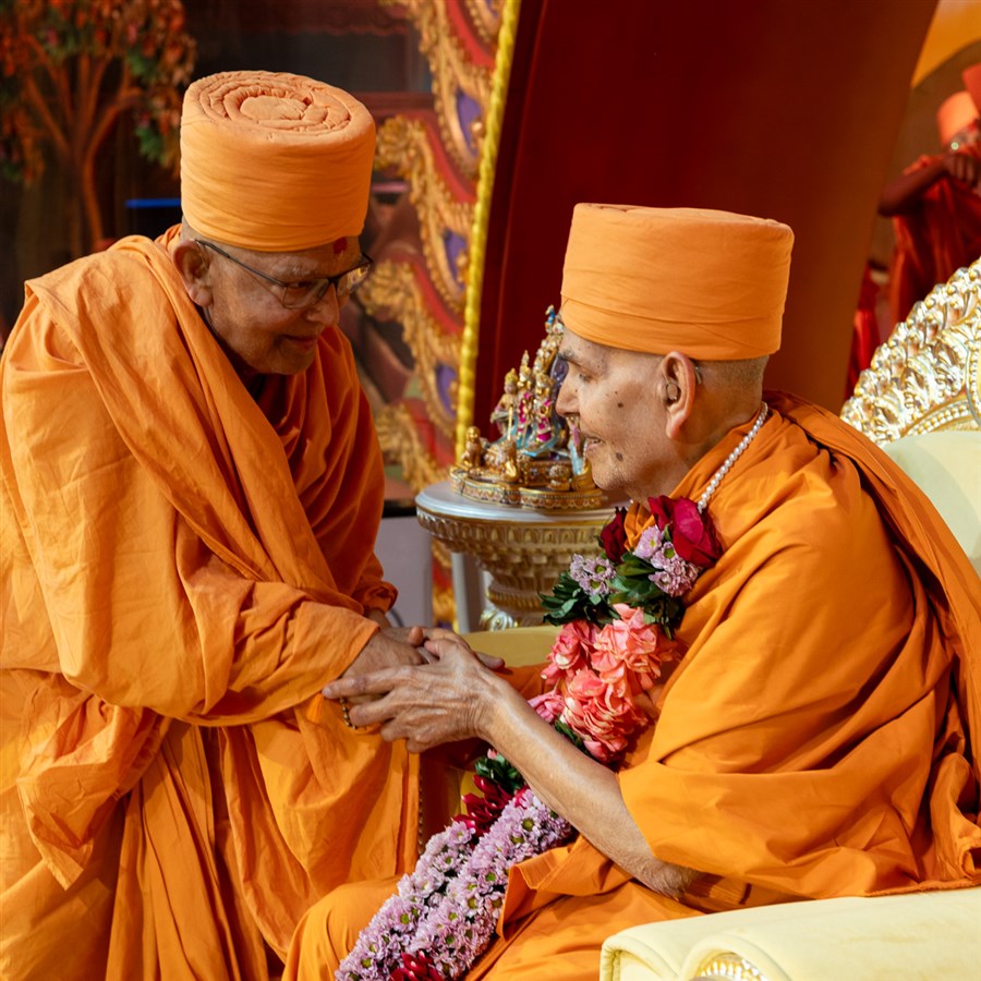 Pujya Ghanshyamcharan Swami honors Swamishri with a garland